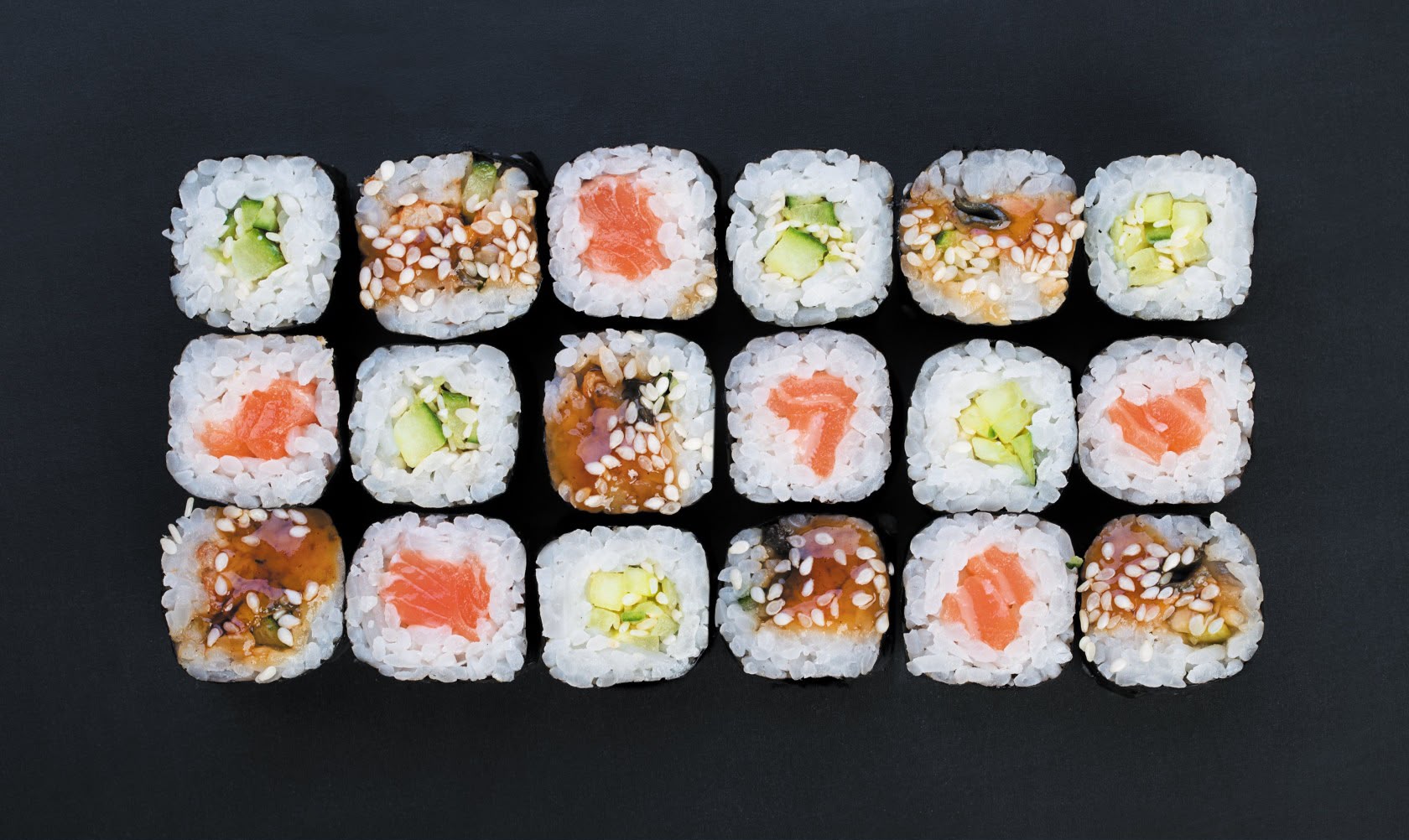 Makis au saumon, concombre et anguille alignés sur fond noir